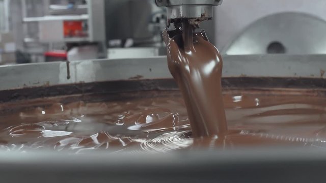 Сhocolate factory, process of pouring fresh chocolate into container, production of sweets and desserts.