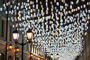 Many bright burning lights blue and yellow lanterns hanging on black night sky background close up, city holiday design illustration, beautiful festive street decoration, celebration decor poster