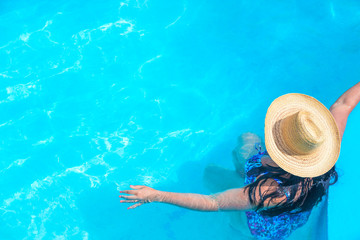 Beautiful sexy woman with straw hat in the blue clear swimming pool with free space. Summer vacation concept.