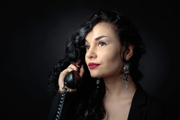Obraz premium Portrait of attractive brunette with old phone on a black bacground.