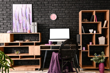 Stylish workplace with modern computer near dark brick wall