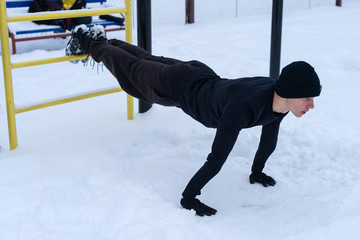 Working out in the snow, guy training on the playground in the winter on the snow