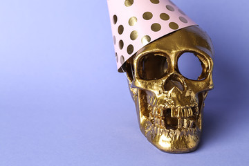 Golden human skull in party hat on color background