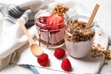 Glass jars of tasty yogurt with jam, strawberry, oatmeal and candied nuts on table