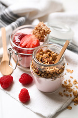 Glass jars of tasty yogurt with jam, strawberry, oatmeal and candied nuts on table