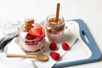 Glass jars of tasty yogurt with jam, strawberry, oatmeal and candied nuts on table