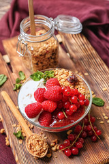 Glass bowl of tasty yogurt with berries and oatmeal on table
