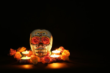 Painted human skull with burning candles and flowers for Mexico's Day of the Dead on dark background