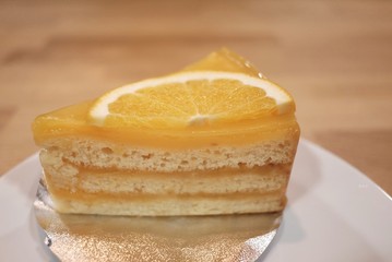 Close up a piece of orange cake on whittle plate with blur wooden dinning background at the coffee cafe 