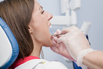 Patient visiting dental office. Adult young brunette woman sitting in chair. Dentist hands in rubber protective gloves working with tools. Check up teeth. Side view. 