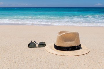 Beach accessories on sand beach for summer vacation, sunglasses and straw hat. Caribbean sea. 