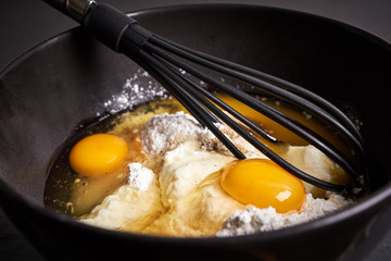 Rührschüssel und Schneebesen mit Eiern, Mehl und Zucker