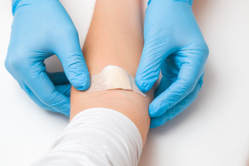 Doctor in blue rubber protective gloves putting an adhesive bandage on young woman's arm vein after blood test or injection of vaccine. First aid. Medical, pharmacy and healthcare concept. Closeup.