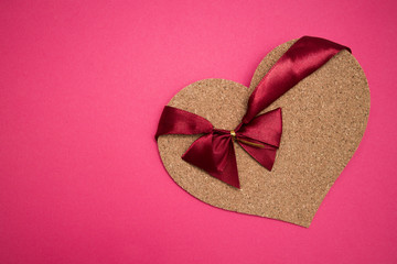 cork heart with red ribbon on it laying on pink background as a symbolof Valentines Day 
