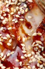 Thin slices of fish are densely covered with a dark, sticky sauce and sprinkled with sesame seeds. Oriental, Chinese, Japanese, Asian dish with soy sauce and grains. Festive snack closeup.