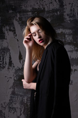 Tender blonde model wearing black jacket posing at studio with shadows