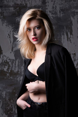 Wonderful blonde model wearing jacket and bra posing at studio with shadows