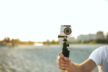 Young man holding an action camera at the desert. Empty space