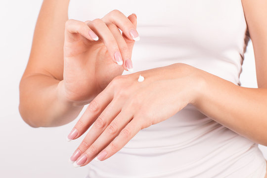 Female hands with french manicure applying hand cream, white background, closeup, front view