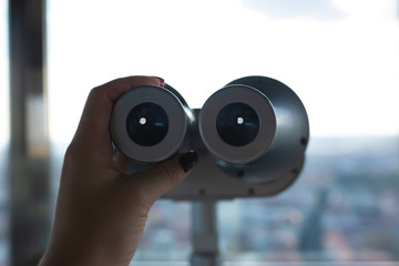 Female hand holding binoculars against the landmark panorama from the observatory