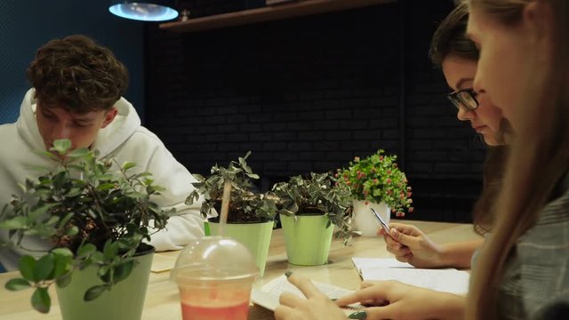 Young guy passes the smoothie to his friend, and then moves back to the girl and continues to read the book with her