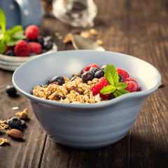 Oat granola with berries and yoghurt in blue bowl on dark old wooden background. Copy space. Healthy breakfast concept.
