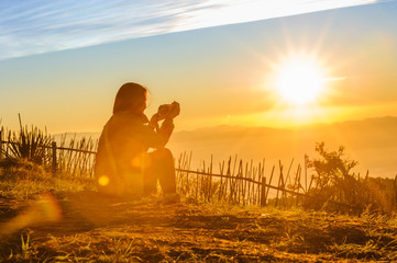 silhouette of female traveler taking photo of beautiful sunrise and mountains with blue sky  in the morning, chiang mai in thailand