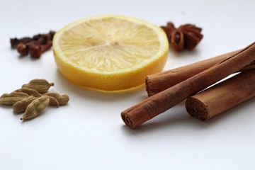 Textured ripe slice of citrus sour lemon, along with fragrant Indian spices of cardamom, cloves and sticks of cinnamon on a white background.