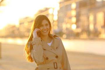 Obraz premium Happy lady talking on phone at sunset in a town