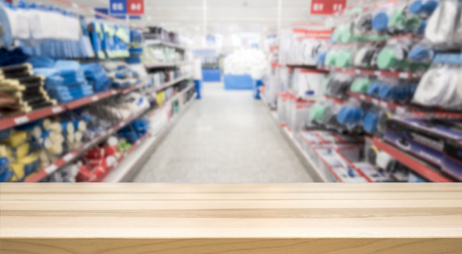 Wooden table top in front of blurred hardware and grocery store. Background for product display montage. Copy space design.