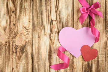 Pink ribbon and bow with pink paper valentine card on wooden background.