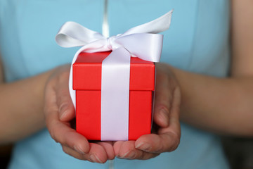 Red gift box in female hands close up. Woman holding present tied with white ribbon, concept of birthday, surprise or Valentine's day