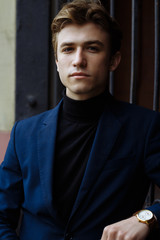 portrait of an attractive man, guy, businessman, looking at the camera, wearing a blue suit, holding a gold watch.