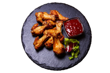 Grilled chicken legs (drumsticks) on a black board isolated on white background. Served with ketchup and lettuce. Top view