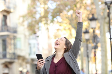 Excited woman holding phone and raising arm in the street