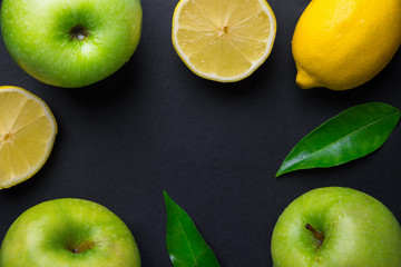 Frame composition from fresh raw green organic apples juicy lemons leaves on black background. Healthy lifestyle vitamins detox balanced diet clean eating vegan concept. Copy space