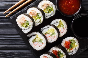 Set of japanese rolls futomaki with soy and chili sauces close-up on a slate board. horizontal top...