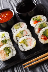 Japanese futomaki rolls with various fillings served with soy and chili sauces close-up on a slate board. vertical