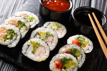 Set of japanese rolls futomaki with soy and chili sauces close-up on a slate board. horizontal