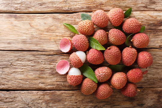 Ripe lychee fruits with green leaves close-up on wooden. Horizontal top view