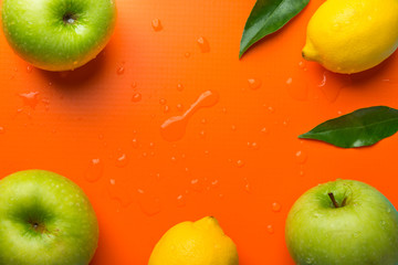 Frame composition from fresh raw green organic apples juicy lemons leaves on orange background. Healthy lifestyle vitamins detox balanced diet clean eating vegan concept. Copy space