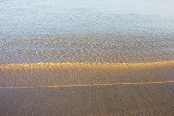 The texture of sand in the flickering light of the coastal waves at sunset. Well suited for creating textures, printing panels and abstract interior posters.