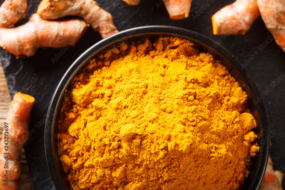 Wall mural ground fresh turmeric in a bowl and root close-up. horizontal top view