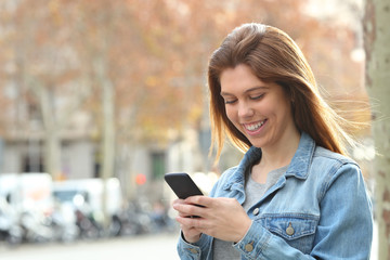 Happy teenager texting on phone walking in the street