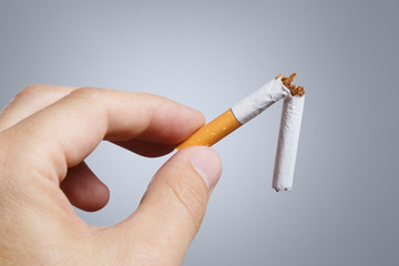 Close-up of fingers holding a cigarette broken in hal on grey background