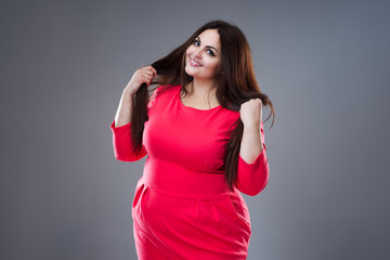 Happy plus size fashion model in red dress, sexy fat woman on gray background