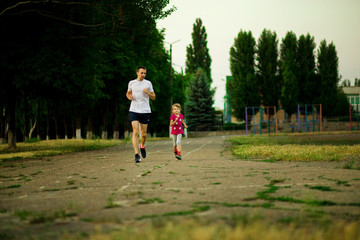 Athletic young father and little daughter running in stadium at sunset.