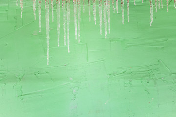 A lot of frozen icicles against the background of a green wall