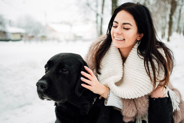 beautiful young girl with black hair in fur coat in winter outdoors, woman with big dog .snowy frosty day