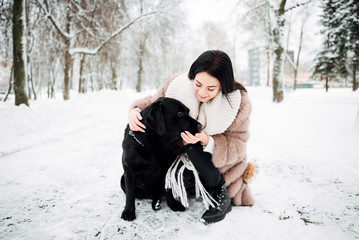 beautiful young girl with black hair in fur coat in winter outdoors, woman with big dog .snowy frosty day